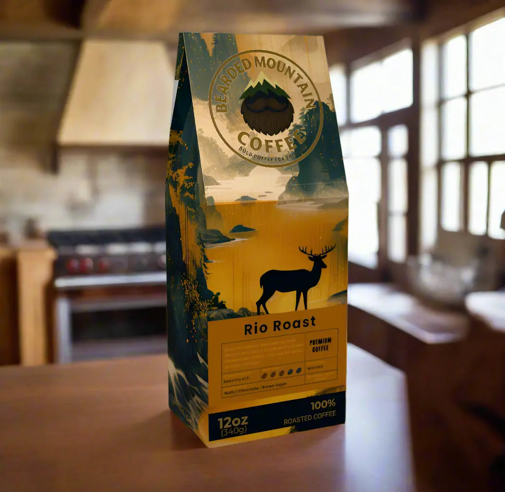 Bearded Mountain Coffee Rio Roast 12oz bag of premium medium roast Brazilian single origin coffee sitting on a rustic wooden kitchen table inside a rugged mountain cabin. The packaging is bold in yellow and deep blue, featuring a silhouette of a stag with antlers against a scenic mountain landscape, symbolizing strength and wilderness. Sunlight streams through large cabin windows, casting natural light across wood countertops, heavy timber cabinets, and a stone stove in the background, creating a masculine,